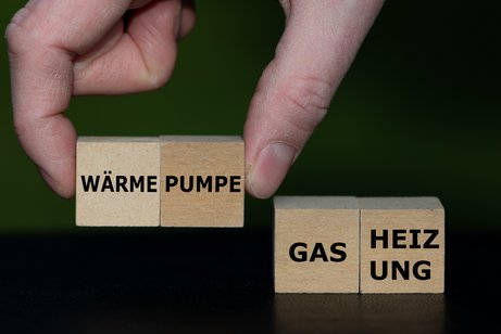 Eine Hand setzt Holzw&uuml;rfel mit W&ouml;rtern zusammen, sie bilden die Worte "W&auml;rme-Pumpe" und "Gas-Heizung"