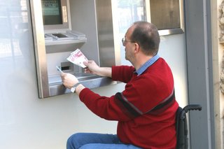 Ein Rollstuhlfahrer hebt Geld am Bankautomaten ab. 