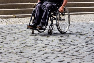 Mann im Rollstuhl auf einem gepflasterten Weg vor einer Treppe 