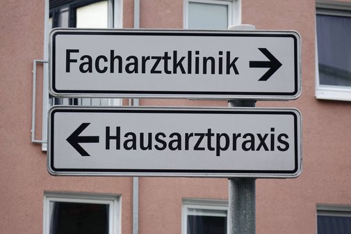 Hausarzt als erste Anlaufstelle Ein Wegweiser mit zwei Schildern. Der eine zeigt nach rechts mit der Aufschrift "Facharztklinik", der andere nach links mit der Aufschrift "Hausarztpraxis"