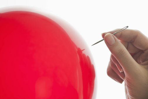 Ein roter Luftballon, eine Hand, die eine Nadel h&auml;lt, n&auml;hert sich.