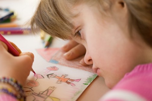 Nahaufnahme eines M&auml;dchens mit Down-Syndrom, das an einem Tisch sitzt und ein Bild malt.