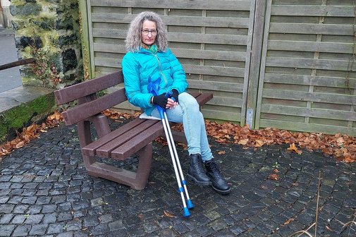 Tanja Groß, Betroffene Stiff-Person-Syndrom Tanja Groß sitzt im Freien auf einer Bank, neben sich ihre Krücken.