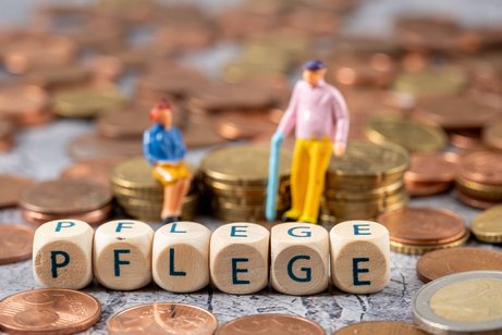 Teure Pflege Seniorenfigürchen sitzen auf Münzstapeln, davor bilden Buchstabenwürfel das Wort Pflege