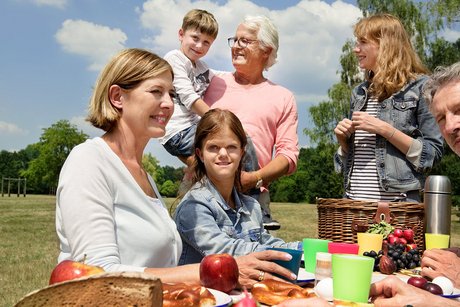 Unterschiedliche Menschen - alt und jung, Männer und Frauen, mit und ohne Behinderung - sitzen draußen auf Bierbänken an einem Tisch, essen gemeinsam.