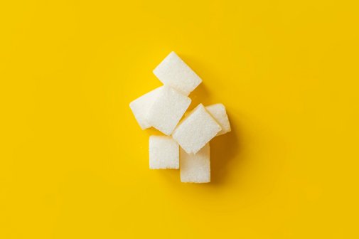 Zuckerkonsum Ein kleiner Berg aus Zuckerwürfeln vor gelbem Hintergrund