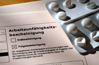 Eine (Folge-)Arbeitsunfähigkeitsbescheinigung vom Hausarzt für eine kranken Arbeitnehmer, daneben ein Tabletten-Blister