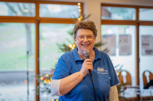 Hannelore Gruszczynski bei einer Veranstaltung, sie hält ein Mikrofon in der Hand. Im Hintergrund sieht man einen Weihnachtsbaum.