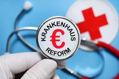 Die Bildmontage zeigt eine Hand mit medizinischem Handschuh, die eine Stethoskop hält, in dessen Mitte das Wort "Krankenhausreform" und ein Euro-Zeichen stehen. 