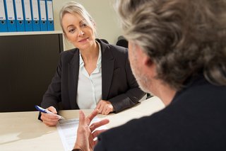 Eine Frau reicht einem Mann eine VdK-Beitrittserklärung. Sie sitzen sich in einem Büro gegenüber, im Hintergrund stehen viele Aktenordner im Regal. 