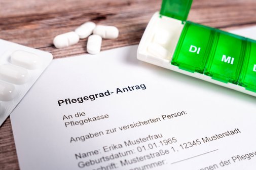Antrag auf Pflegegrad Ein ausgedruckter Muster-Antrag auf einen Pflegegrad, daneben liegen Tabletten-Blister und eine Pillenbox