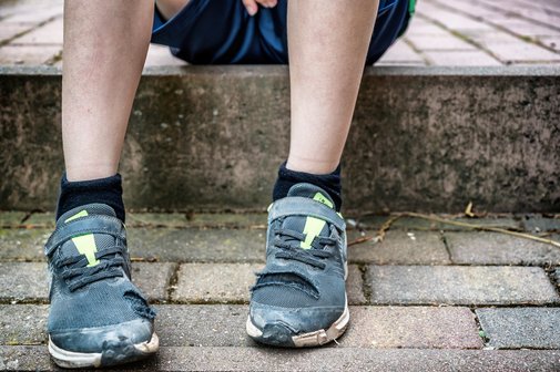 Armut und Wohngeldkürzung Ein Junge sitzt auf einem Bordstein, seine Turnschuhe sind abgenutzt und stellenweise kaputt.