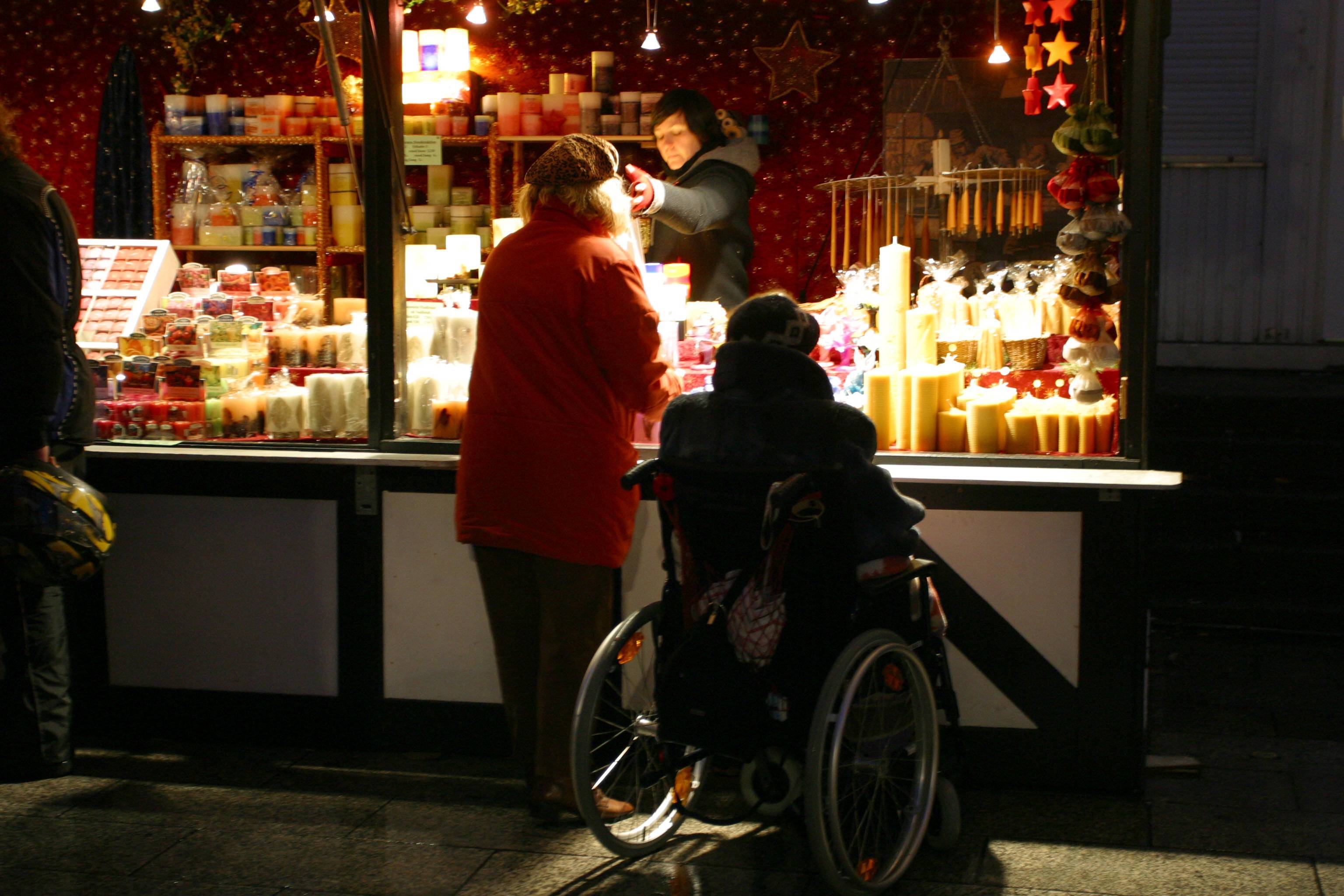 Ein älterer Mann im Rollstuhl und eine ältere Frau an einem Kerzenstand auf dem Weihnachtsmarkt am Breitscheidplatz in Berlin