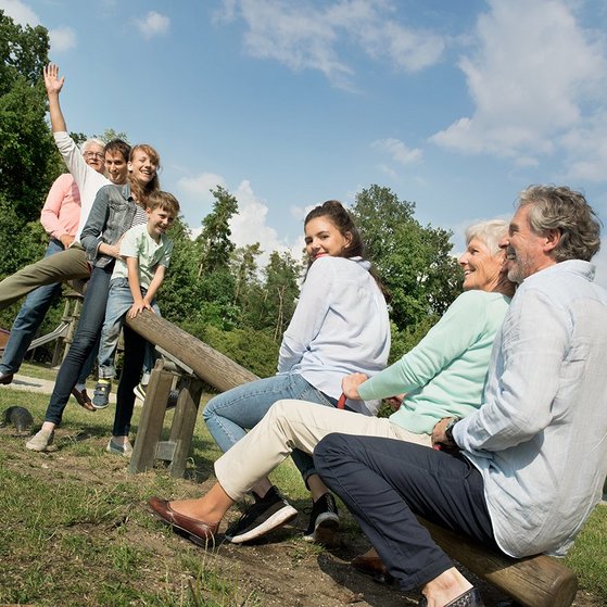 Junge und alte Menschen und ein Kind sitzen auf einer Wippe auf einem Spielplatz Junge und alte Menschen und ein Kind sitzen auf einer Wippe auf einem Spielplatz